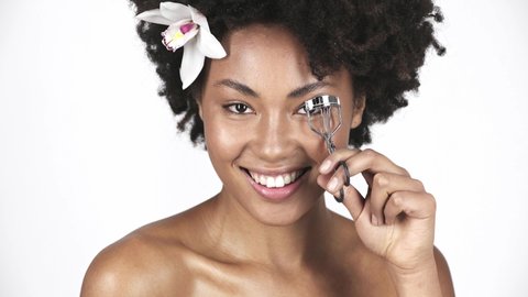 attractive african american woman smiling and using eyelash curler on white