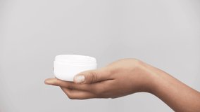 cropped view of african american girl holding container and taking cosmetic cream isolated on grey