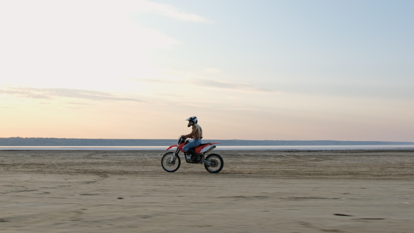 A sportswoman doing stunts on a sports bike as she rides at speed along the wide beach of the lake.
