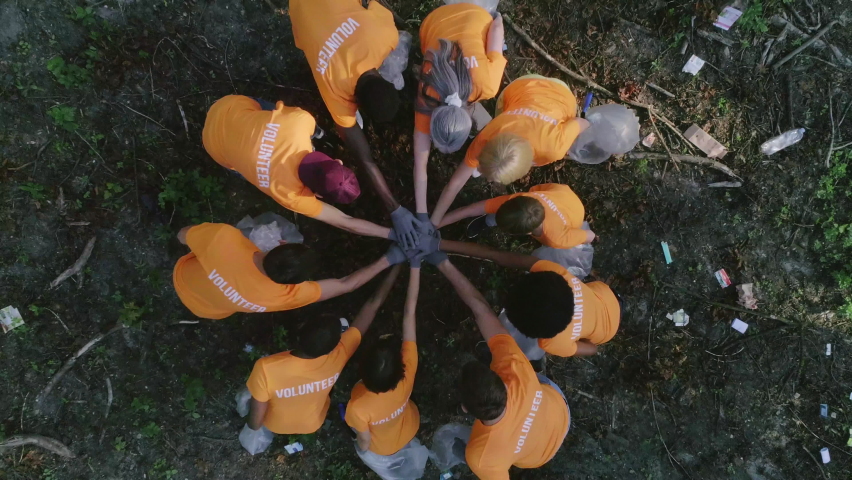 Aerial top view of people in gloves putting hands together and applouding. Eco activists spreading out in forest and collecting litter. Concept of teamwork, nature pollution. Royalty-Free Stock Footage #1070169979