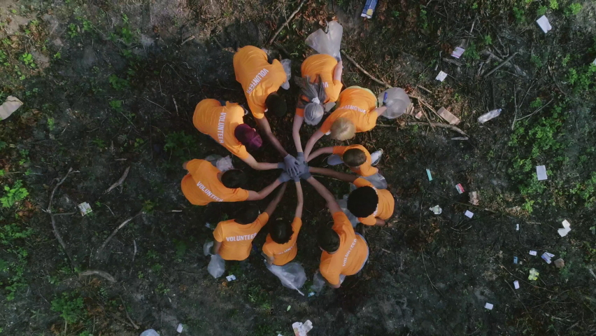 Aerial top view of people in gloves putting hands together and applouding. Eco activists spreading out in forest and collecting litter. Concept of teamwork, nature pollution. | Shutterstock HD Video #1070169979