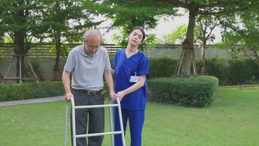 Asian young woman nurse at nursing home taking care disable senior elderly man. Caregiver doctor serve physical therapy for older patient to exercise and practice walking on walker or cane at backyard | Shutterstock HD Video #1070175760