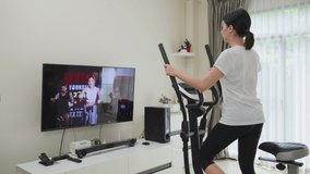 Asian Sport woman workout exercising by watching fitness live or video tutorial TV online on laptop at home. Young Girl in casual using exercise bikes follow instruction from trainer during quarantine