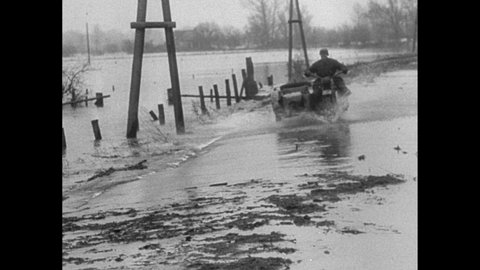 1950s Germany: Rushing water, flooded land, collapsed dike, water gauge, man rides motorcycle with sidecar. Leafless trees, ruins of building.