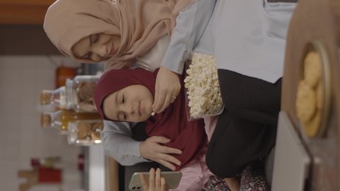 Mother is having a good time with her daughter.A mother and her daughter in a turban make a video call over their cell phone while eating popcorn.  Fun concept together.Video for the vertical story.