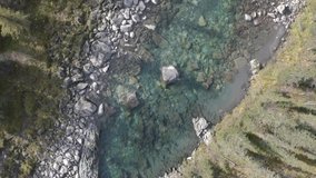Aerial top view of a blue cold river flowing through summer green forest and stones. Clip. Nature landscape with stone mountainous stream and trees.