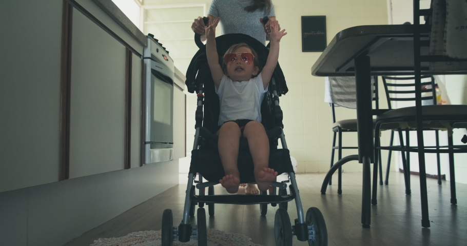 Family have fun in room. Mother gives her toddler girl a ride on the baby stroller along the rooms in apartment