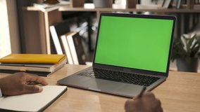 Man looking at chroma key green screen laptop computer in living room watching movie, video content. Online education. Over shoulder close up view. Business man working from home office. Template 4K