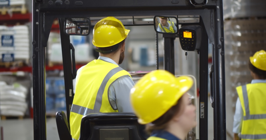Portrait young male warehouse worker sitting in forklift truck and smiling at camera. Happy forklift driver looking at camera working in large industrial storehouse Royalty-Free Stock Footage #1070187571