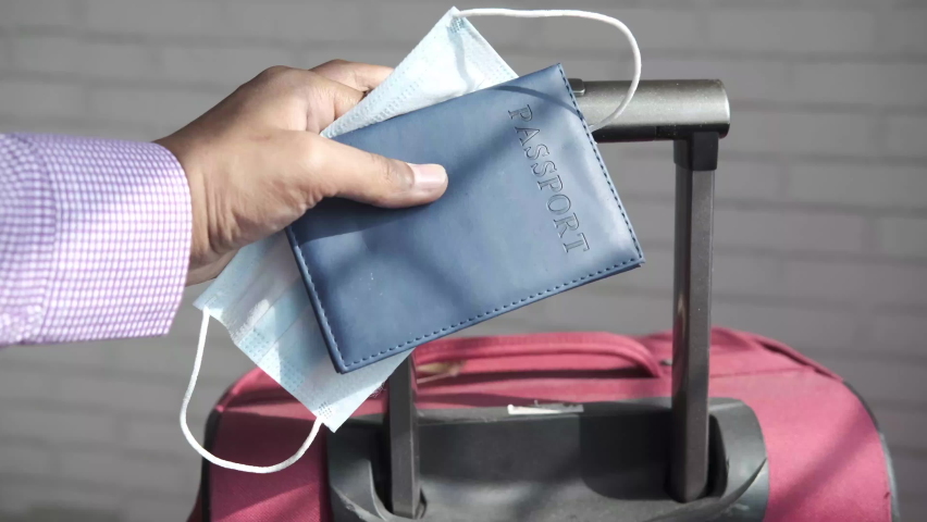 holding passport in hand with suitcase on ground 