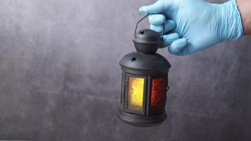 hand in gloves holding lantern light against black background .