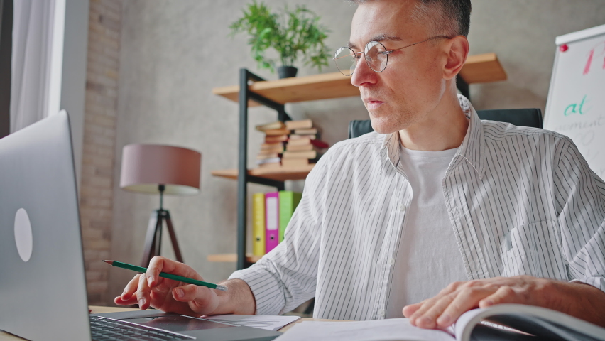 Middle aged man having troubles with using computer, reading manual book and feeling despair, taking off his eyeglasses