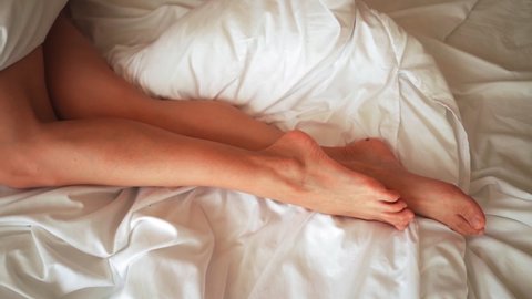 Beautiful female legs gracefully move in bed in the morning. Body care concept. Top view.