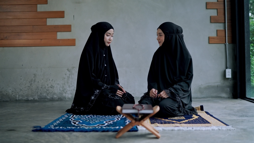 Locked shot, Young muslim woman and sister wears traditional black clothes sitting on mat, they makes traditional greeting with smile in prayer room at home