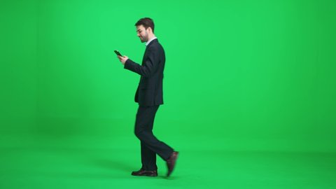 Passer-by man in a suit walks on a green background and uses a smartphone, template on a chromakey.