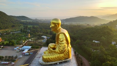 4k Aerial: The golden image of Luang Phor Thuat, the most famous and respected monk in Thailand. Big Golden Statue in mountains at beautiful sunrise in Khao Yai, Korat province Aerial
