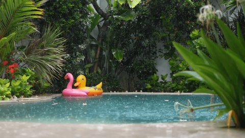 Rain season. Lonely giant inflatable floats in the private swimming pool of tropical villa 