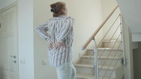 Portrait of caucasian woman having low back pain while walking up the stairs