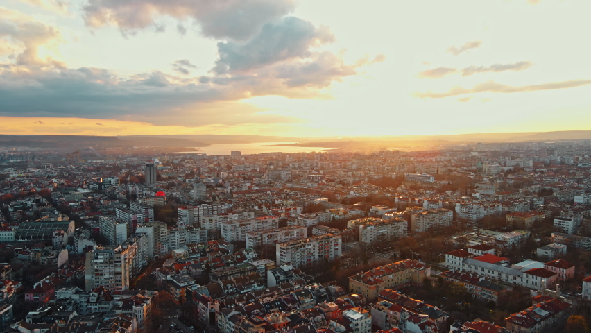 Aerial View Shot of Panorama city by Sea at Orange Sunset Clouds in Spring day against blue sky drone. Maritime city port aerial view city ​​buildings houses. Shooting from drone. Urban. Lens flares