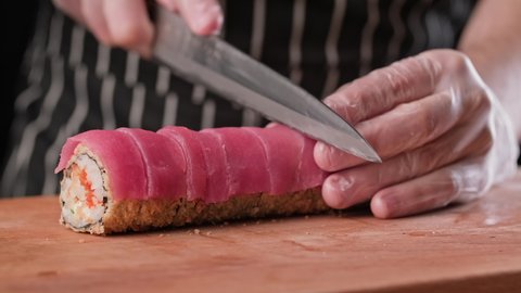 Chef cutting sushi rolls with knife. Process of cooking sushi maki. Close-up of male chef preparing asian food. Tempura sushi with tuna, shrimp, caviar. 4K, UHD