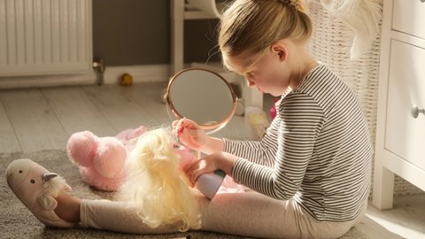 Little child girl paints eyes with eyeshadow her doll playing make makeup in the children's room. Imitates adults make up artist experiments with cosmetics.