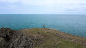 Aerial video with a woman tourist with a backpack taking pictures with her mobile phone of a picturesque rocky coastline surrounded by turquoise sea waters, Black Sea coast