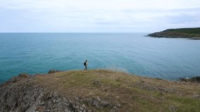 Aerial video with a female tourist with a backpack walking on a picturesque rocky coastline surrounded by turquoise sea waters, Black Sea coast