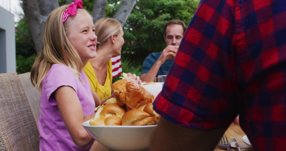 Smiling caucasian girl eating at family celebration meal in garden. family celebrating eating outdoors together.