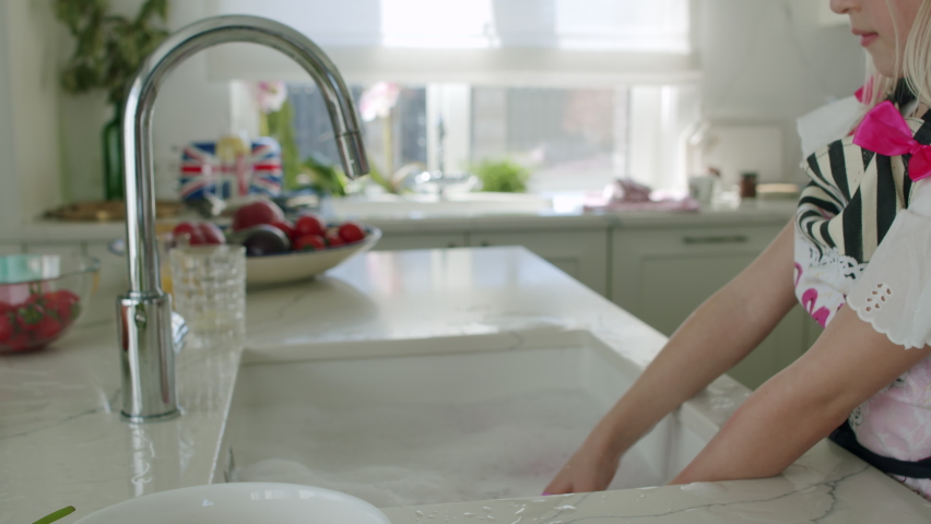 Caucasian girl washing having fun in kitchen. Child helping her mom. Slow motion 4K UHD video 50 fps
