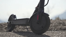 Man starting a ride on electric kick scooter or e-scooter against mountain landscape background. Close up motion. Electric transportation concept. Closeup footage