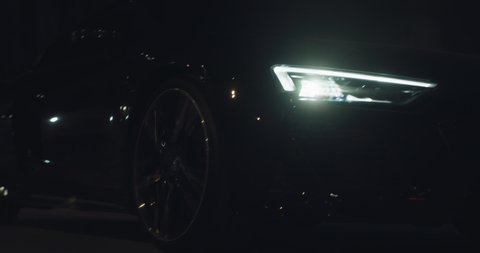 Cinematic close up shot of modern racing car with switched on headlights running on race track at night. Concept of passion for driving cars and engines,auto dealership, luxury cars, speed and power.