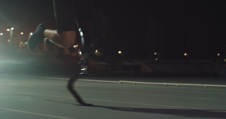 Cinematic close up of disable man with legs prosthesis running with effort with racing auto behind on car track at night. Concept of handicapped people active lifestyle, determination, motivation. | Shutterstock HD Video #1070233609