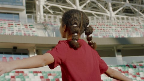 Portrait of African American Black child girl walking onto the field of huge soccer football stadium, spreading hands, dreaming of becoming professional player, soccer star. Women sport concept