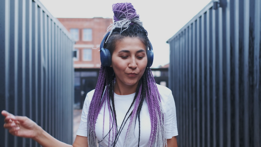 Happy Young Female Student Celebrating Successful Exams Finish Outdoor. Pretty Joyful Girl with Dyed Dreadlocks Dancing and Having Fun while Enjoying Music in Headphones. Looking in Camera, closeup. Royalty-Free Stock Footage #1070235532
