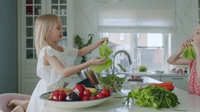 Smart girl preparing salad. Caucasian sisters show beard and ears made from lettuce leaves. Side view portrait of family team having fun In kitchen. Slow motion 4K UHD video 50 fps
