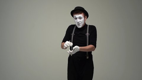 Portrait of male mime flipping imaginary coin, remains dissatisfied with result and flips coin again, after repeated failure begins to cry. Talented actor showing pantomime against white background.