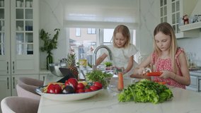 Smart girl preparing salad, peeling carrot. Caucasian sisters wash strawberries, vegetables in the sink under tap water. Sisters chat with family or friends online . Slow motion 4K UHD video 50 fps