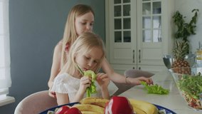 Smart girl preparing salad. Caucasian sisters eat lettuce leaves and onion. Portrait of children having fun In kitchen. Slow motion 4K UHD video 50 fps