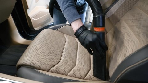 Man hoovering a car cabin using vacuum cleaner on a front seat inside the car.