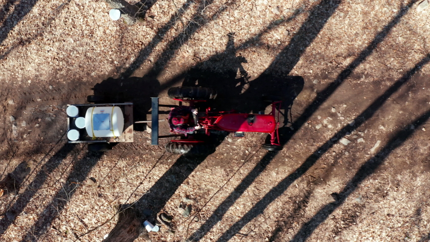 Red Tractor Driving Down Trails Collecting Sap From Maple Trees For Sugar Shack in Quebec Canada to Process into Maple Syrup. 4k Aerial Drone Shot Royalty-Free Stock Footage #1070252506