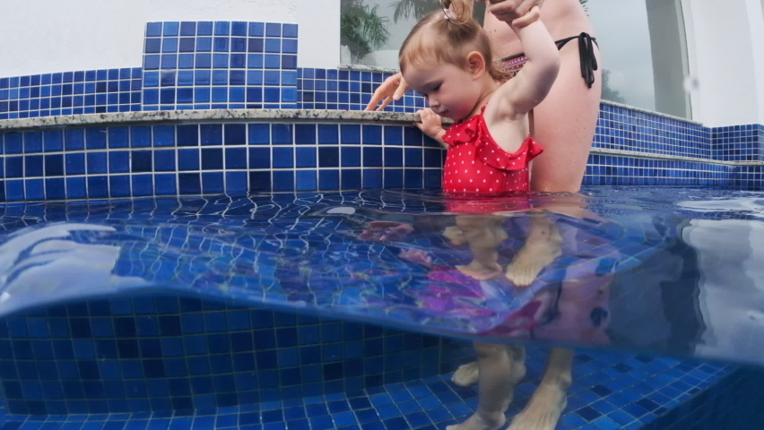 Woman walks with toddler girl in the swimming pool