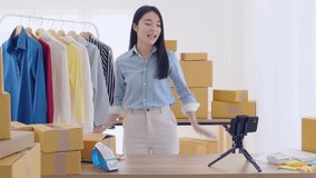 Young asian woman ,clothing store small business owner, showing clothes in front of camera to recording vlog video live streaming at her shop.Business online on social media concept. 