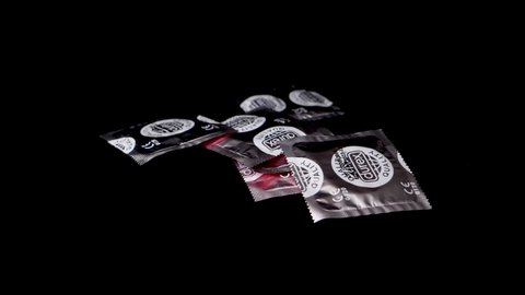 Bilten , Switzerland - 03 17 2021: Silver condom packs are thrown on black surface in slow motion.