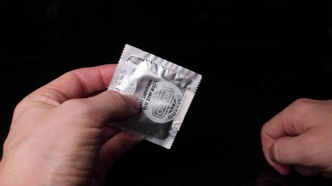 Bilten , Switzerland - 03 17 2021: Caucasian hands opening a condom pack and takes out a condom.