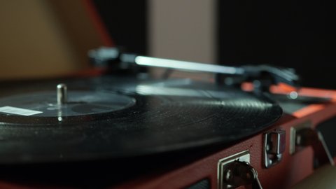 Woman hand adjusts the head old record player and vinyl discs at home. Using vinyl audio player. Music lover listens to classical music. Red device. Close up