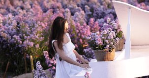Girl in white dress play piano in flowers garden at Chiang mai Thailand footage 4K video slow motion summer holiday traveling concept 
