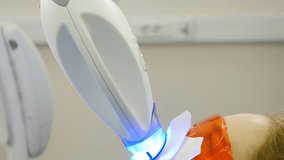 Professional teeth whitening or bleaching procedure in modern dental clinic. Patient in protective glasses while LED whitening. Ultraviolet rays. lamp for teeth enamel whitening. 4K video