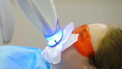 Professional teeth whitening or bleaching procedure in modern dental clinic. Patient in protective glasses while LED whitening. Ultraviolet rays. lamp for teeth enamel whitening. 4K video