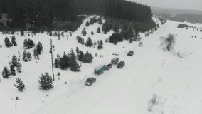 Aerial view of winter coniferous forest. Clip. snow falling on a rural road with parked cars near snow covered white field.