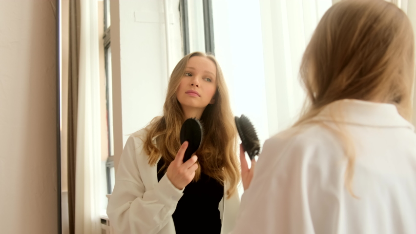 Young woman has problems with combing brushing her dry damaged hair with difficulty in mirror. Hard to style tangled hair. | Shutterstock HD Video #1070278879